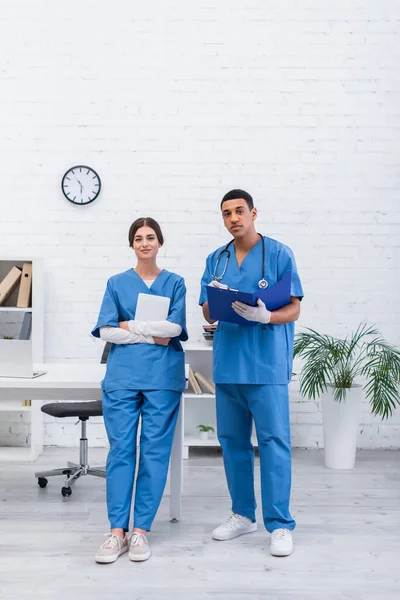 Médecins vétérinaires Interracial tenant tablette numérique et presse-papiers dans la clinique — Photo de stock