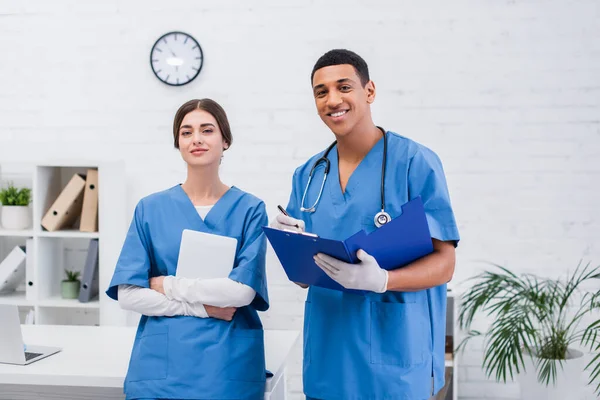 Positive multiethnic vet doctors holding clipboard and digital tablet in clinic — Photo de stock