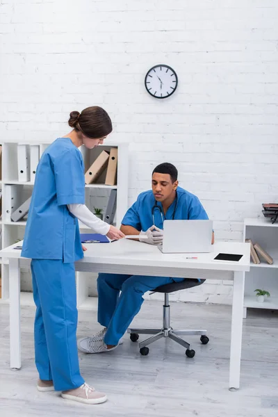 Veterinario sosteniendo escaneo cerca de colega afroamericano y dispositivos en clínica - foto de stock