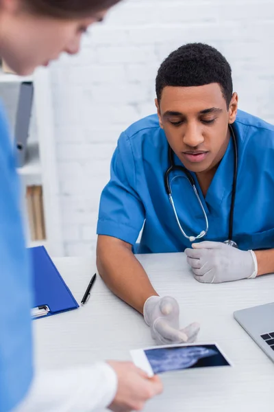 Veterinario afroamericano señalando ecografía borrosa cerca de colega en clínica - foto de stock