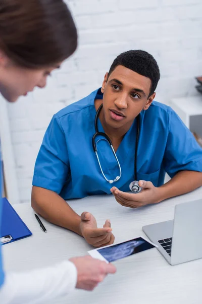 Medico veterinario afroamericano che parla con collega offuscato con ecografia in clinica — Foto stock