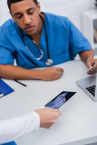 Veterinarian holding ultrasound scan near blurred african american colleague in clinic - foto de stock