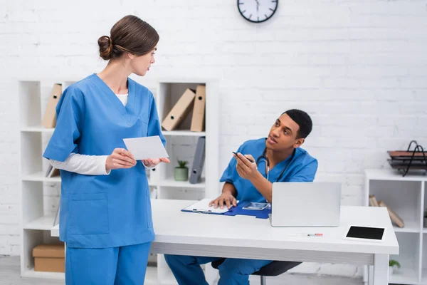 Vet doctor holding scan near blurred african american colleague with clipboard in clinic — Foto stock