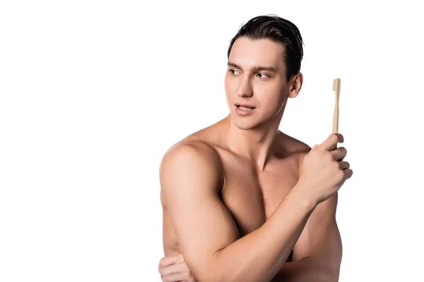 Hombre sin camisa con un cuerpo perfecto sosteniendo el cepillo de dientes y mirando hacia otro lado aislado en blanco - foto de stock