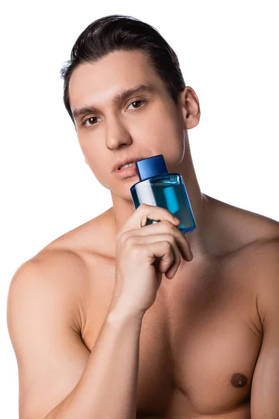 Hombre con pecho desnudo sosteniendo frasco de perfume cerca de la cara aislado en blanco - foto de stock