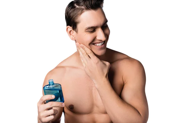 Hombre alegre sin camisa aplicando después de afeitarse loción en la mejilla aislado en blanco — Stock Photo