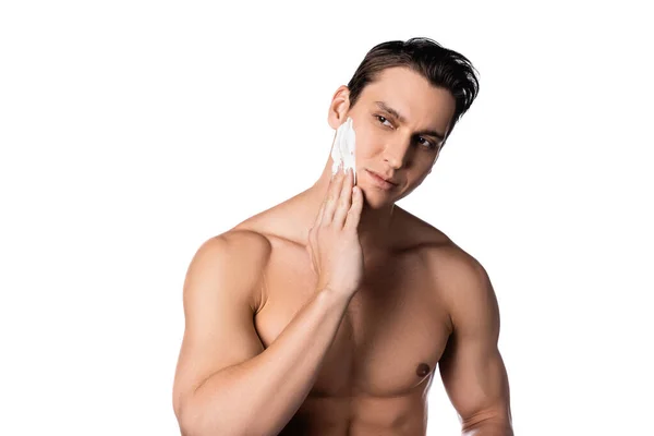 Morena sin camisa hombre aplicando espuma de afeitar y mirando hacia otro lado aislado en blanco - foto de stock
