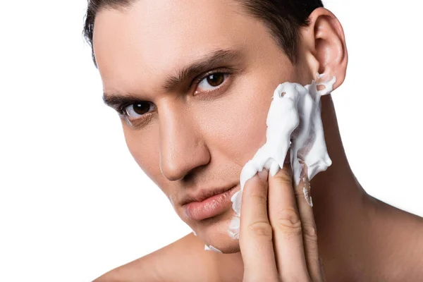 Retrato de hombre morena aplicando espuma de afeitar y mirando a la cámara aislada en blanco - foto de stock