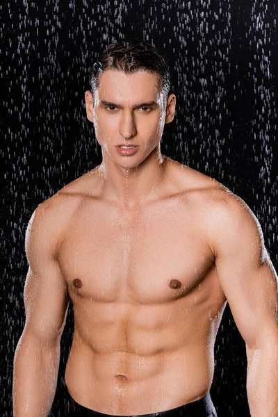 Wet man with muscular torso looking at camera on black background — Stock Photo