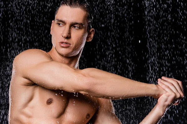 Мускулистый мужчина вытягивает руки под душем на черном фоне — стоковое фото