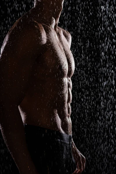 Silhouette eines gestutzten Mannes mit perfektem Körper unter Regen auf schwarzem Hintergrund — Stockfoto