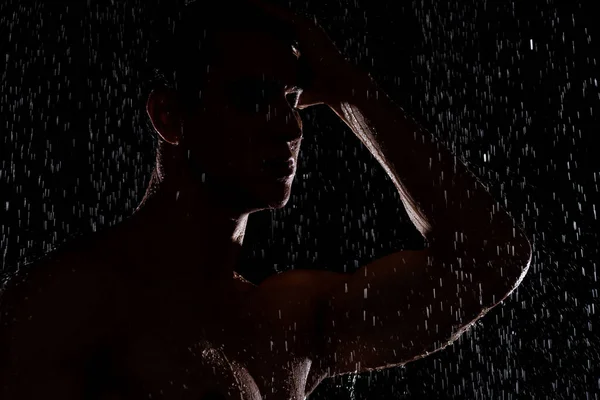Silhouette dell'uomo sotto caduta gocce d'acqua su sfondo nero — Foto stock