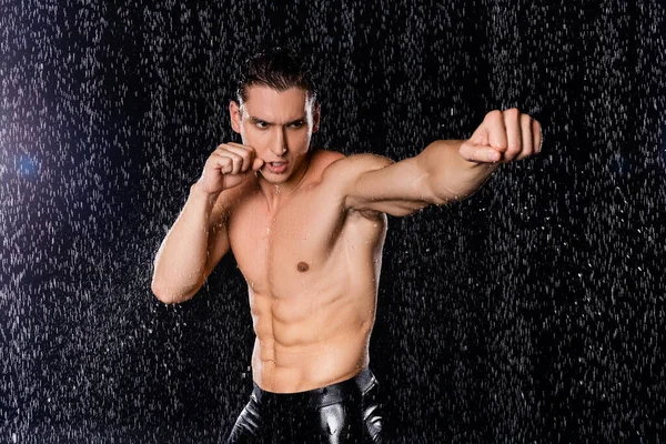 Сильный мужчина с мускулистым туловищем в боксе позирует под дождем на черном фоне — стоковое фото