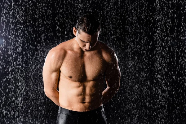 Мужчина с сильным телом, стоящим под дождем с руками сзади на черном фоне — стоковое фото