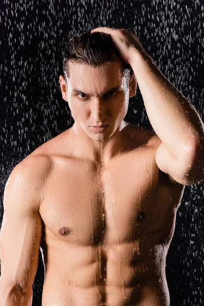 Уверенный человек смотрит на камеру под душем на черном фоне — стоковое фото