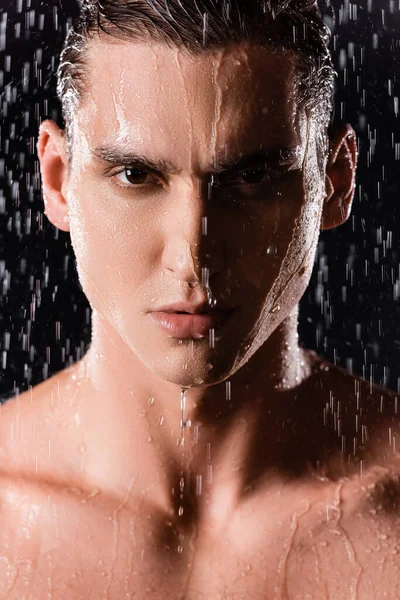 Retrato de homem confiante olhando para a câmera sob gotas de chuva em fundo preto — Fotografia de Stock