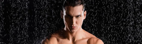 Man with naked shoulders looking at camera under water drops on black background, banner — Stock Photo