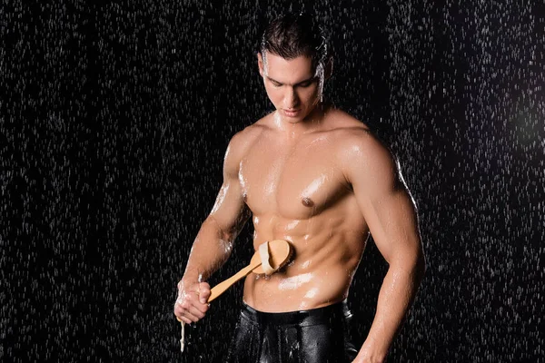 Man washing muscular body with shower brush on black background — Stock Photo