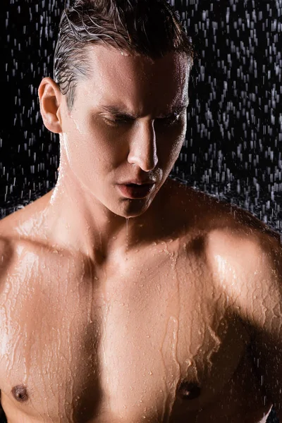 Человек с мускулистой грудью под дождем душ на черном фоне — стоковое фото