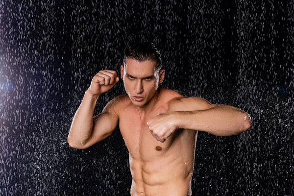 Homem musculoso e confiante em pé no boxe posar sob o chuveiro no fundo preto — Fotografia de Stock