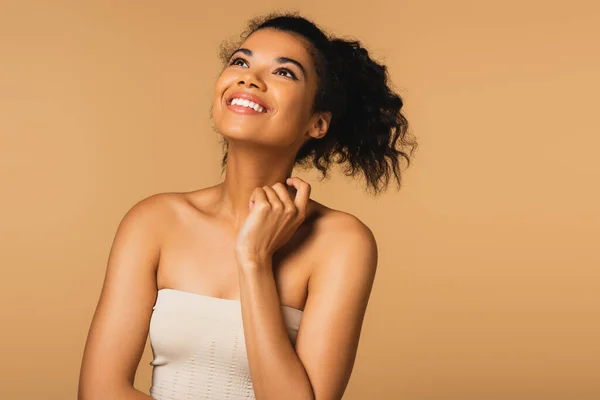 Heureuse jeune femme afro-américaine aux épaules nues regardant isolée sur beige — Photo de stock