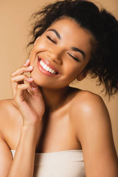 Portrait of pleased african american woman with bare shoulders and closed eyes isolated on beige — Stock Photo