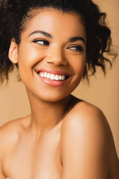 Portrait de femme afro-américaine joyeuse aux épaules nues regardant loin isolé sur beige — Photo de stock