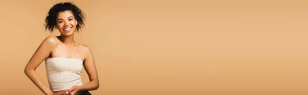 Heureuse femme afro-américaine aux épaules nues et au maquillage naturel isolé sur beige, bannière — Photo de stock