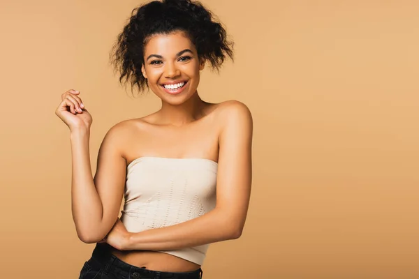 Positive jeune femme afro-américaine avec les épaules nues regardant la caméra isolée sur beige — Photo de stock