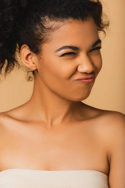 Curly african american woman with bare shoulders grimacing isolated on beige — Stock Photo