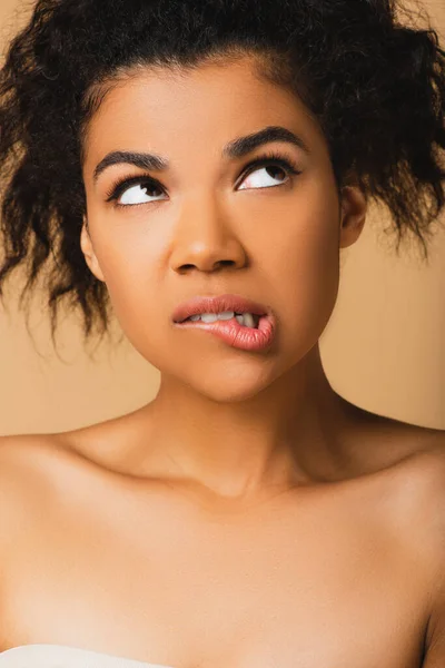 Mujer afroamericana reflexiva con hombros desnudos mirando hacia otro lado aislado en beige - foto de stock