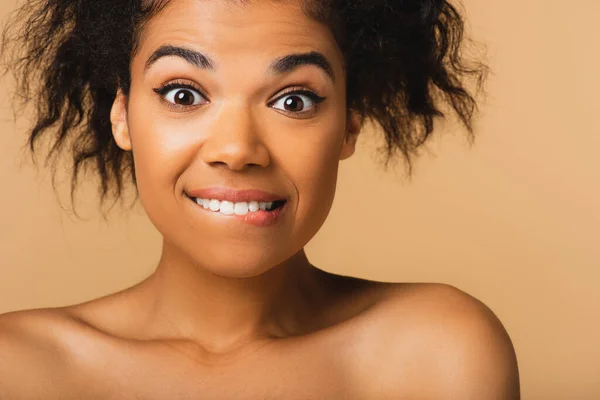 Frisée afro-américaine avec les épaules nues mordant lèvre isolée sur beige — Stock Photo