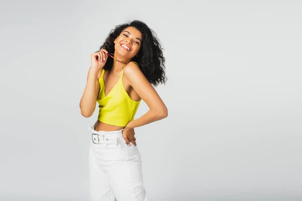 Positive african american woman holding colorful beads and posing with hand on hip isolated on grey — Stock Photo