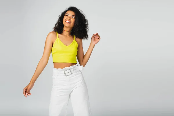 Pleased african american woman in yellow crop top posing while gesturing isolated on grey — Stock Photo