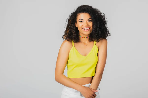 Cheerful african american woman in yellow crop top smiling isolated on grey — Stock Photo