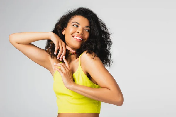 Cheerful african american woman in yellow crop top smiling while posing isolated on grey — Stock Photo
