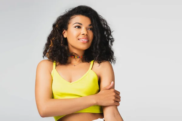 Dreamy african american woman in yellow crop top smiling isolated on grey — Stock Photo