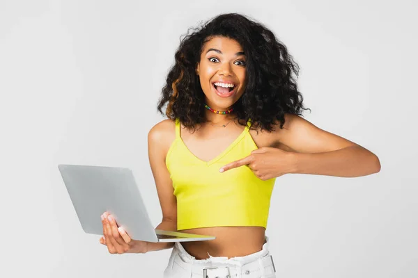 Pigiste afro-américain positif dans le haut de la culture jaune pointant vers ordinateur portable isolé sur gris — Photo de stock