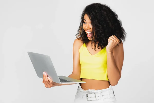 Pigiste afro-américain positif dans le haut de culture jaune à l'aide d'un ordinateur portable isolé sur gris — Photo de stock