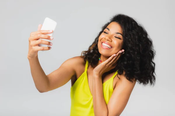 Mujer afroamericana feliz tomando selfie en teléfono inteligente aislado en gris - foto de stock