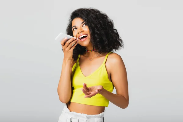Animado afro-americano mulher gravação mensagem de voz enquanto segurando smartphone isolado no cinza — Fotografia de Stock