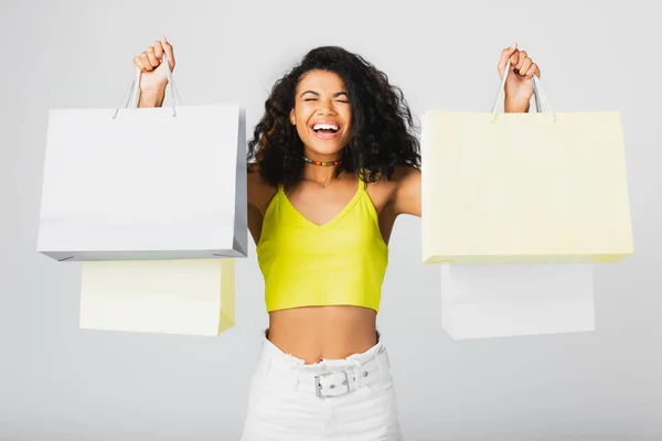 Animado afro-americano mulher segurando sacos de compras isolados em cinza — Fotografia de Stock