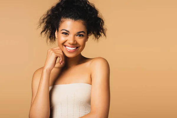 Feliz joven afroamericana mujer con los hombros desnudos mirando a la cámara aislada en beige - foto de stock