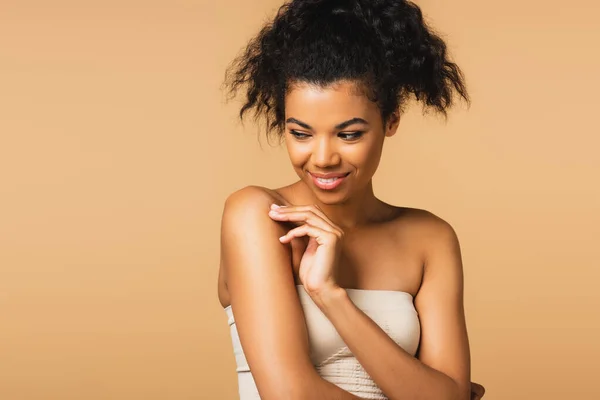 Happy young african american woman with bare shoulders looking away isolated on beige — Stock Photo