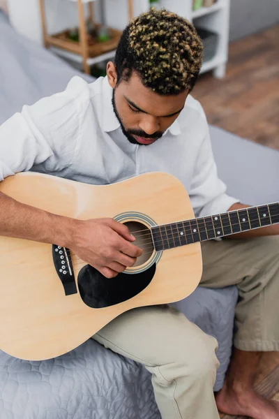 Aus der Vogelperspektive: junger afrikanisch-amerikanischer Mann mit gefärbten Haaren spielt Akustikgitarre im Schlafzimmer — Stockfoto