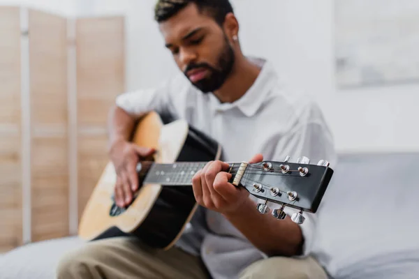 Borrosa joven afroamericano hombre con barba tocando la guitarra acústica en casa — Stock Photo