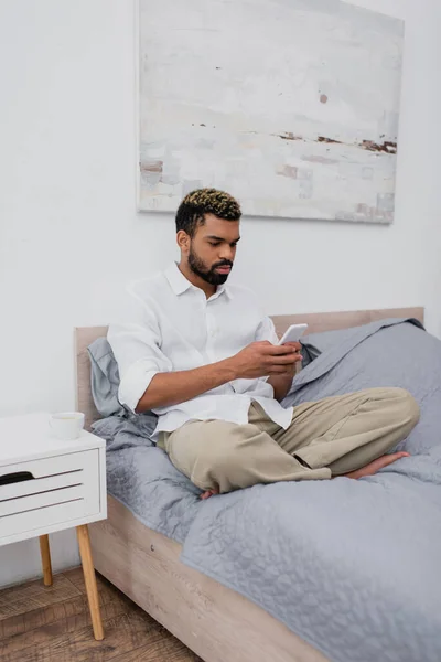 Jovem afro-americano com cabelo tingido usando smartphone enquanto descansa na cama — Fotografia de Stock