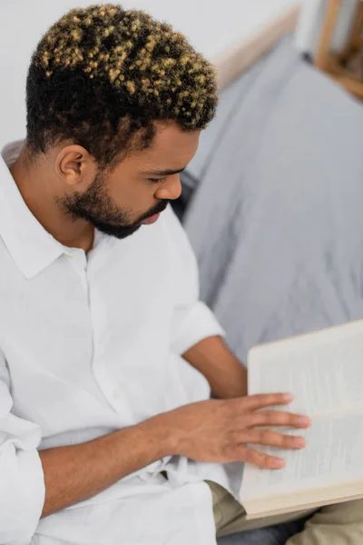 Високий кут зору бородатого афроамериканця з пофарбованим волоссям читання книги в спальні — стокове фото