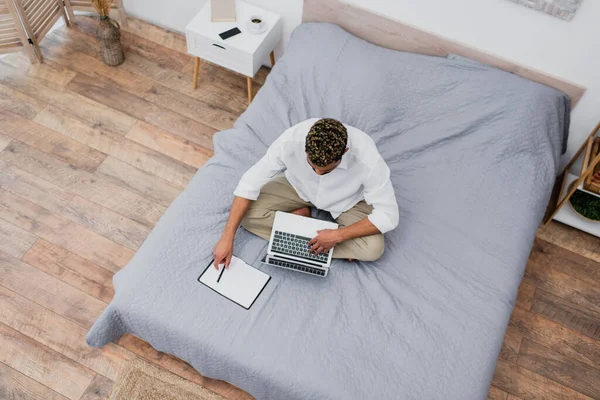 Vista dall'alto del giovane uomo afroamericano con i capelli tinti utilizzando il computer portatile mentre seduto sul letto — Foto stock