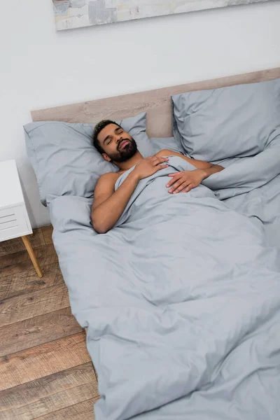 Vue grand angle de jeune homme afro-américain avec les yeux fermés dormant au lit — Photo de stock